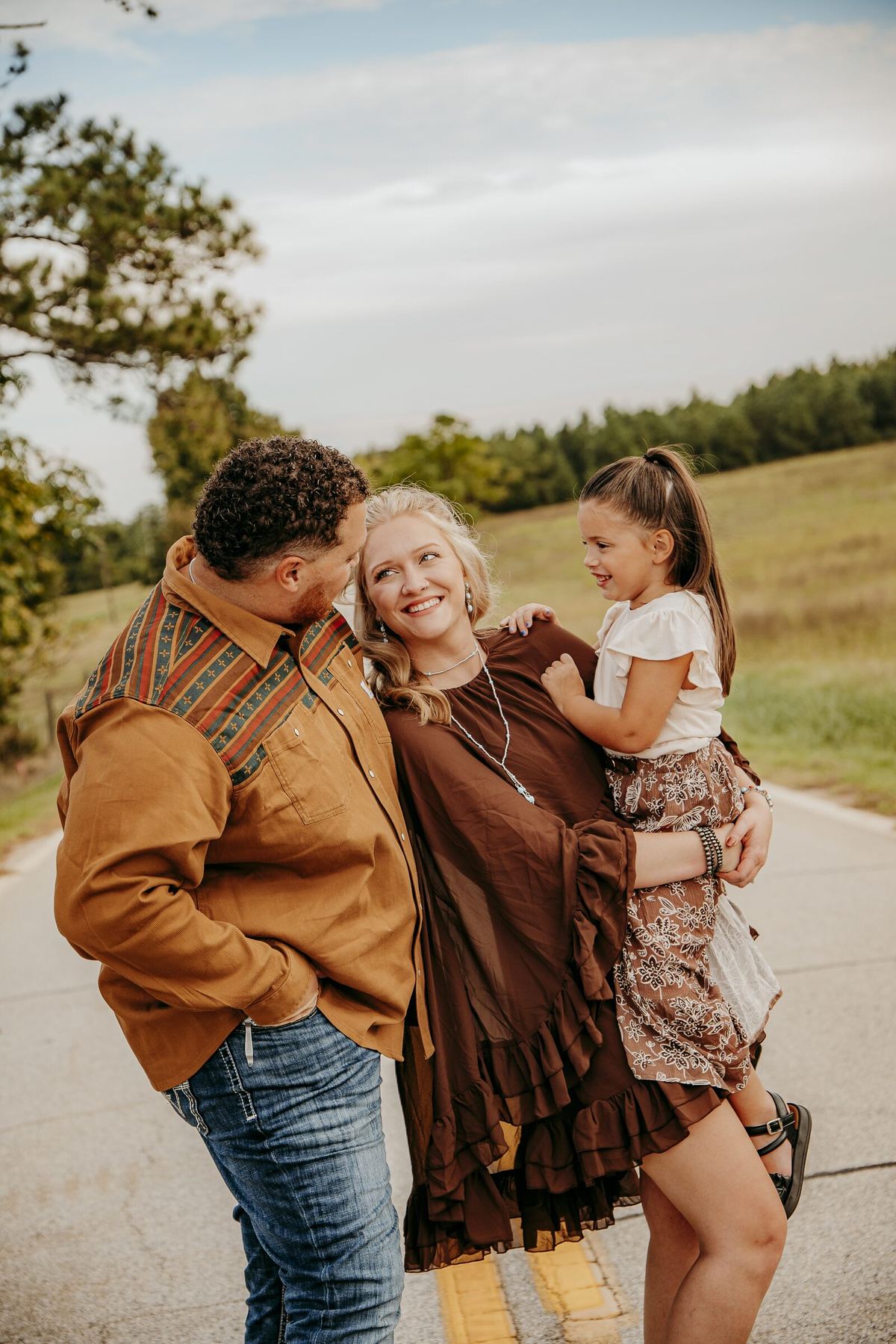 Family photography session with mom, dad, and daughter on a country road